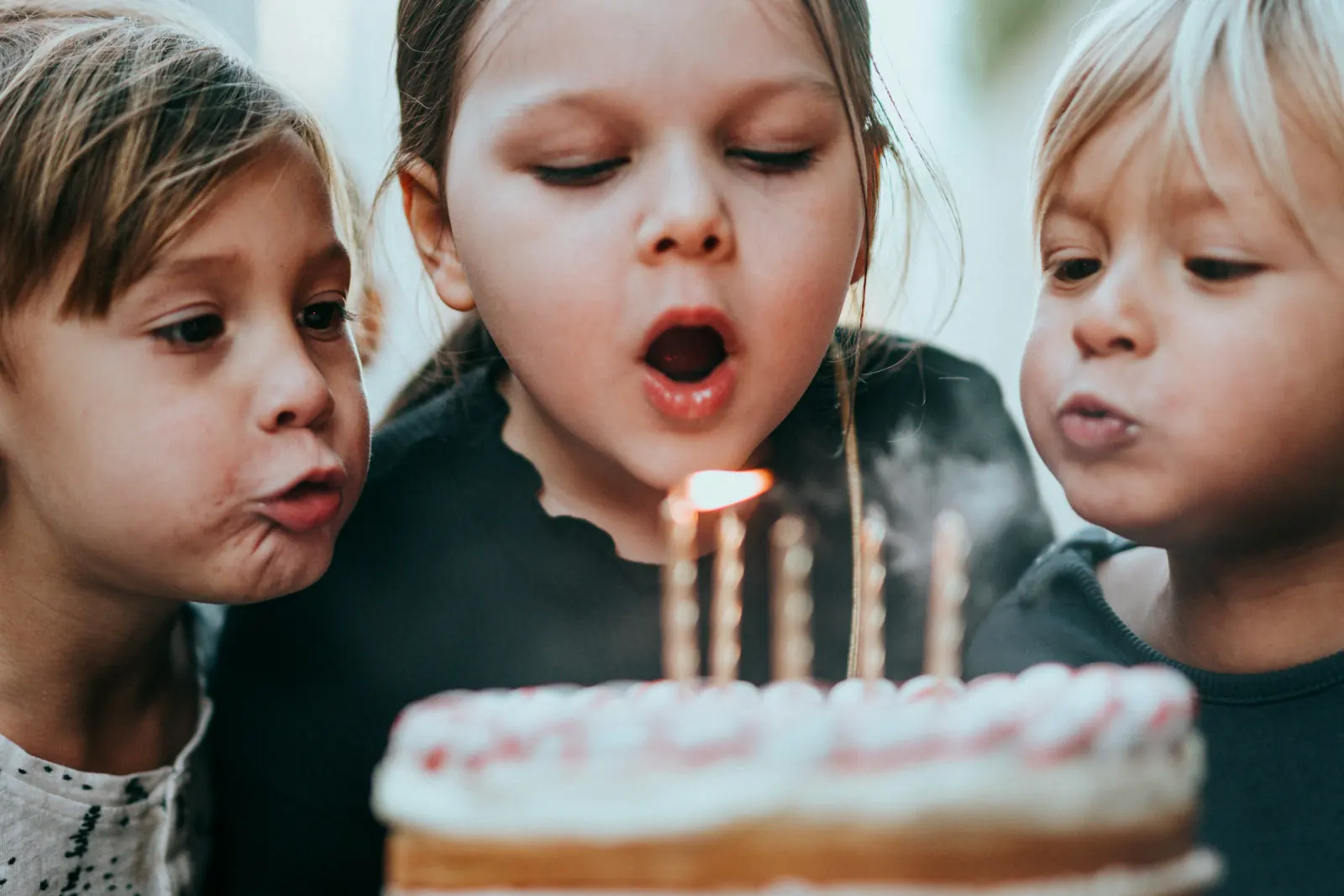 Three children blowing out the candles on a birthday cake