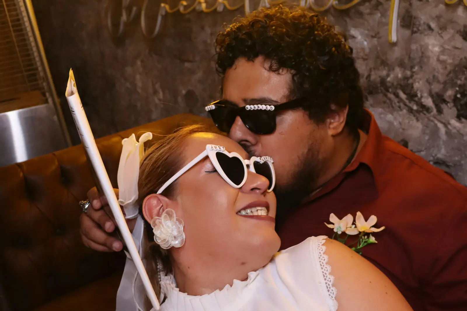 Newlyweds in heart-shaped sunglasses sharing a kiss with photo booth props
